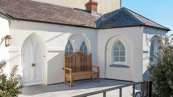 A white building with a wooden bench, arched windows, and a tiled roof.