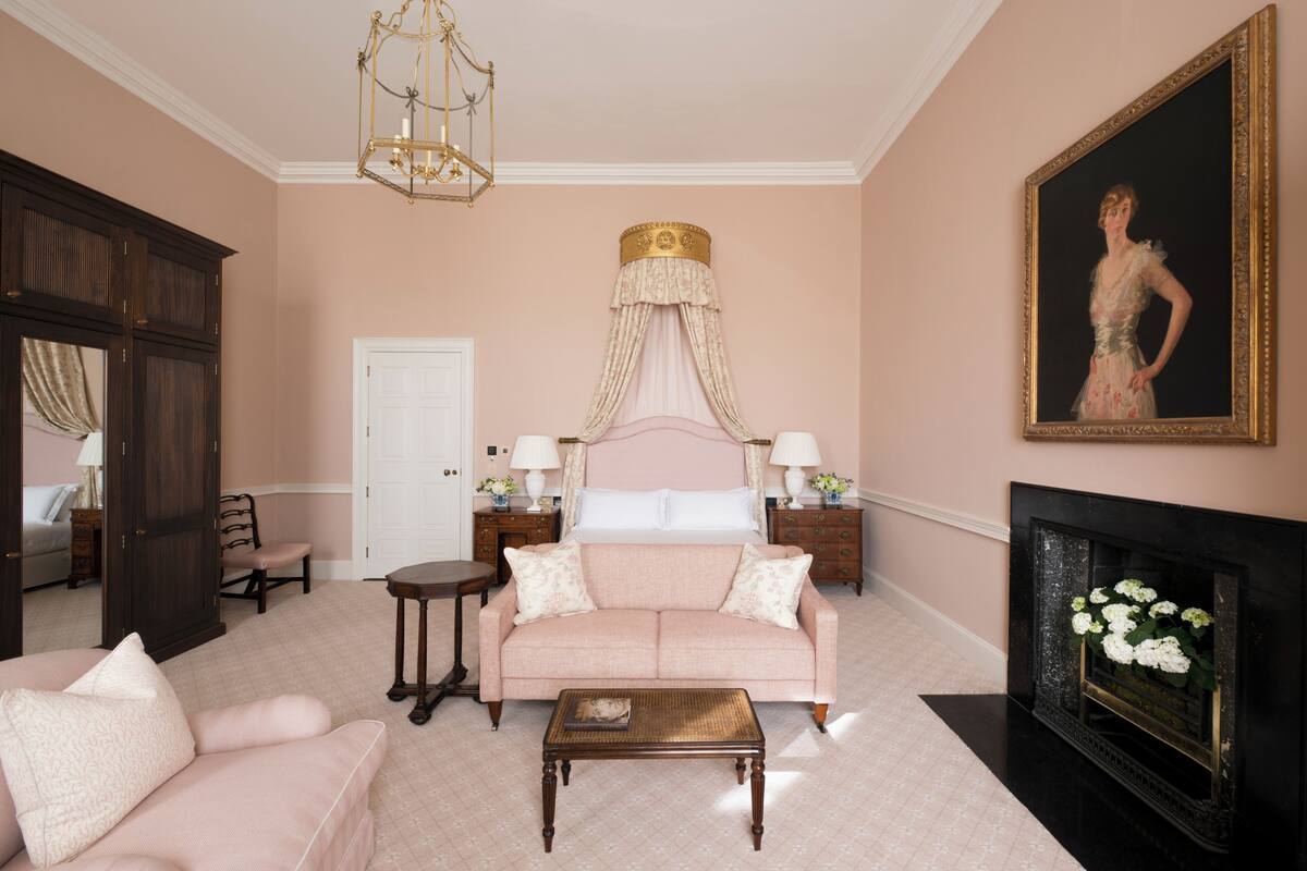 Een slaapkamer met een groot bed, een zithoek met een bank en fauteuil, een open haard en een schilderij aan de muur.