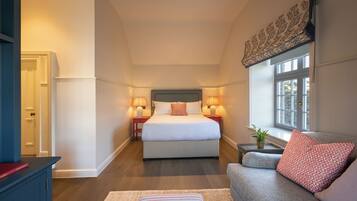 A bedroom with a large bed, bedside lamps, a window with a view, and a sofa with a patterned pillow.