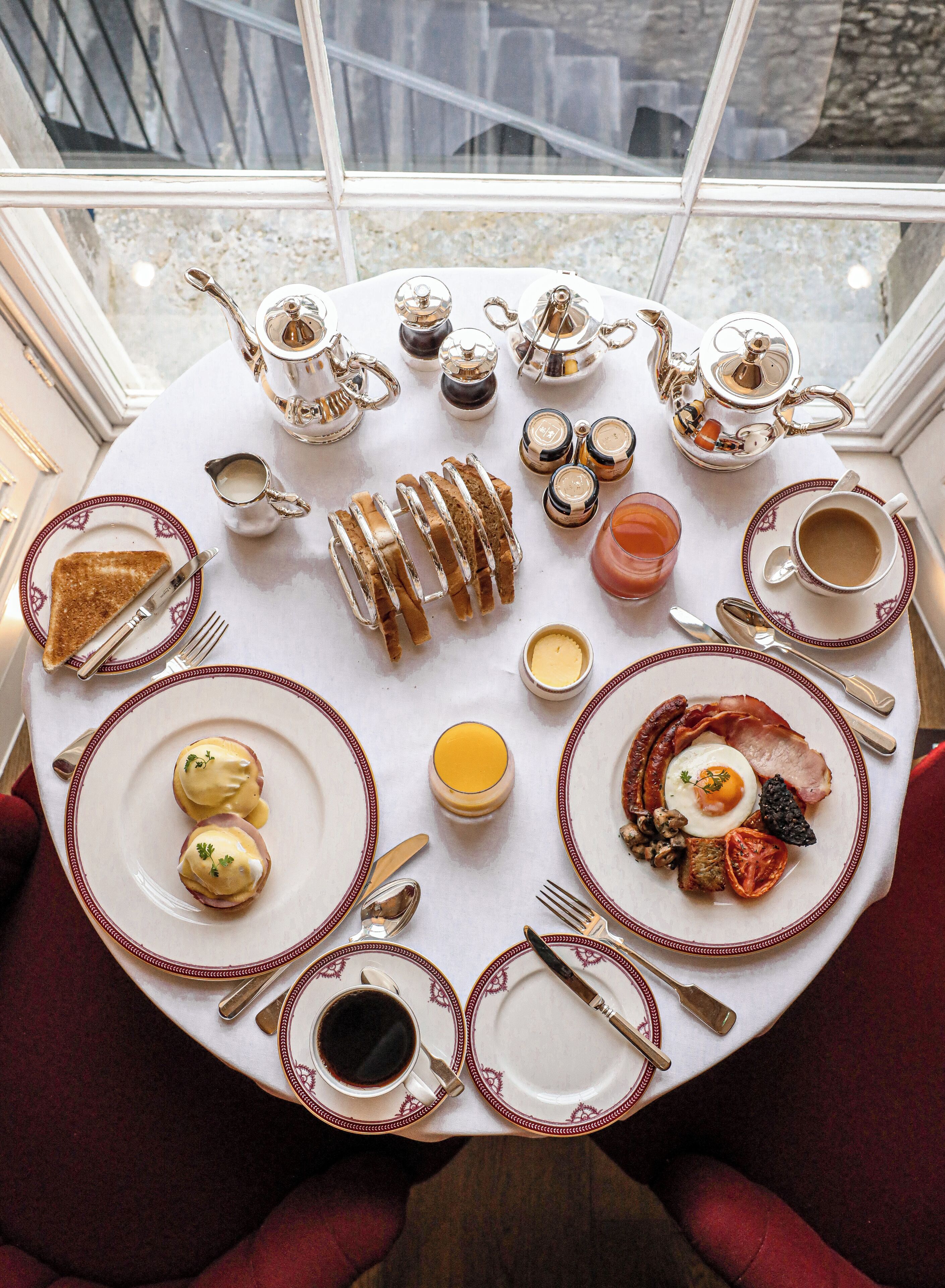 A breakfast setting with a variety of dishes, including toast, eggs, bacon, and coffee, arranged on a round table.