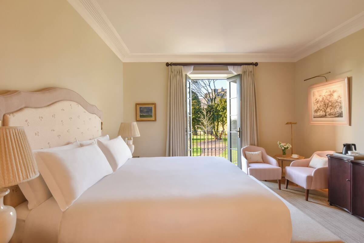Een hotelkamer met een groot bed, twee fauteuils, een bijzettafeltje en uitzicht op het omliggende landschap.