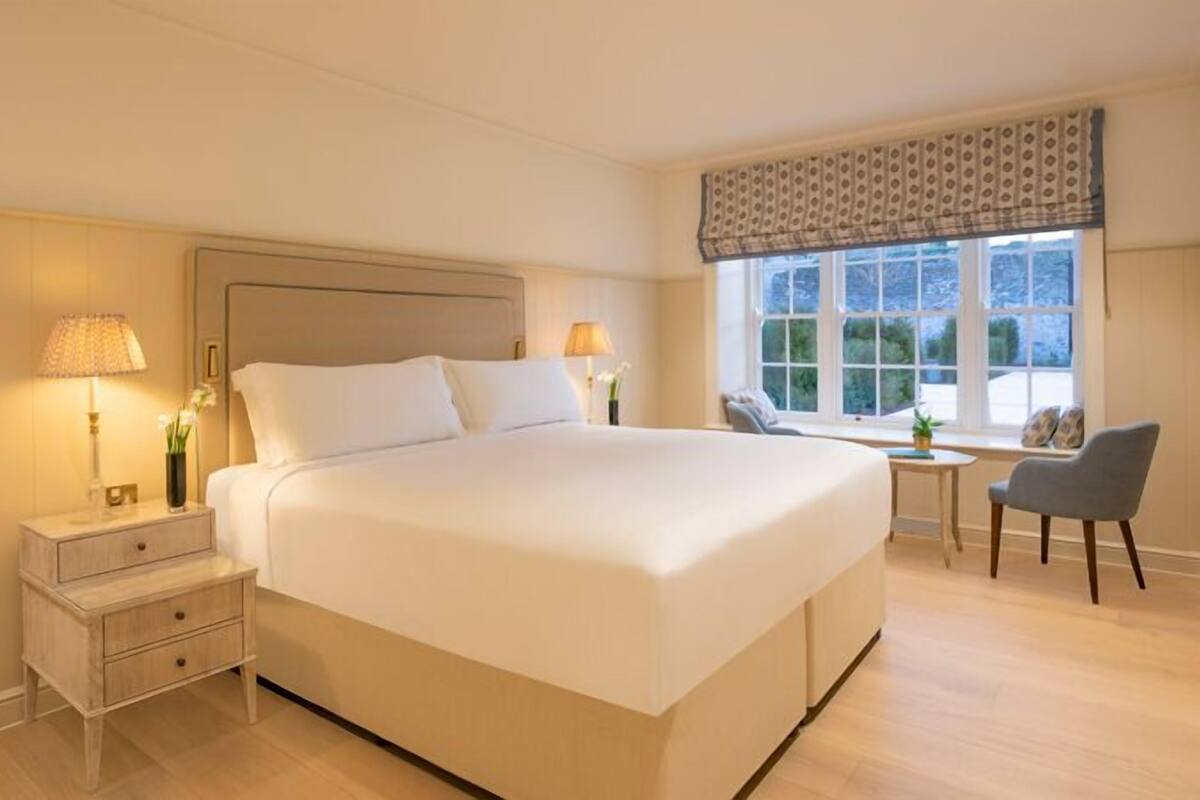 Een hotelkamer met een groot bed, nachtkastjes, een stoel, een klein tafeltje en een raam met uitzicht.