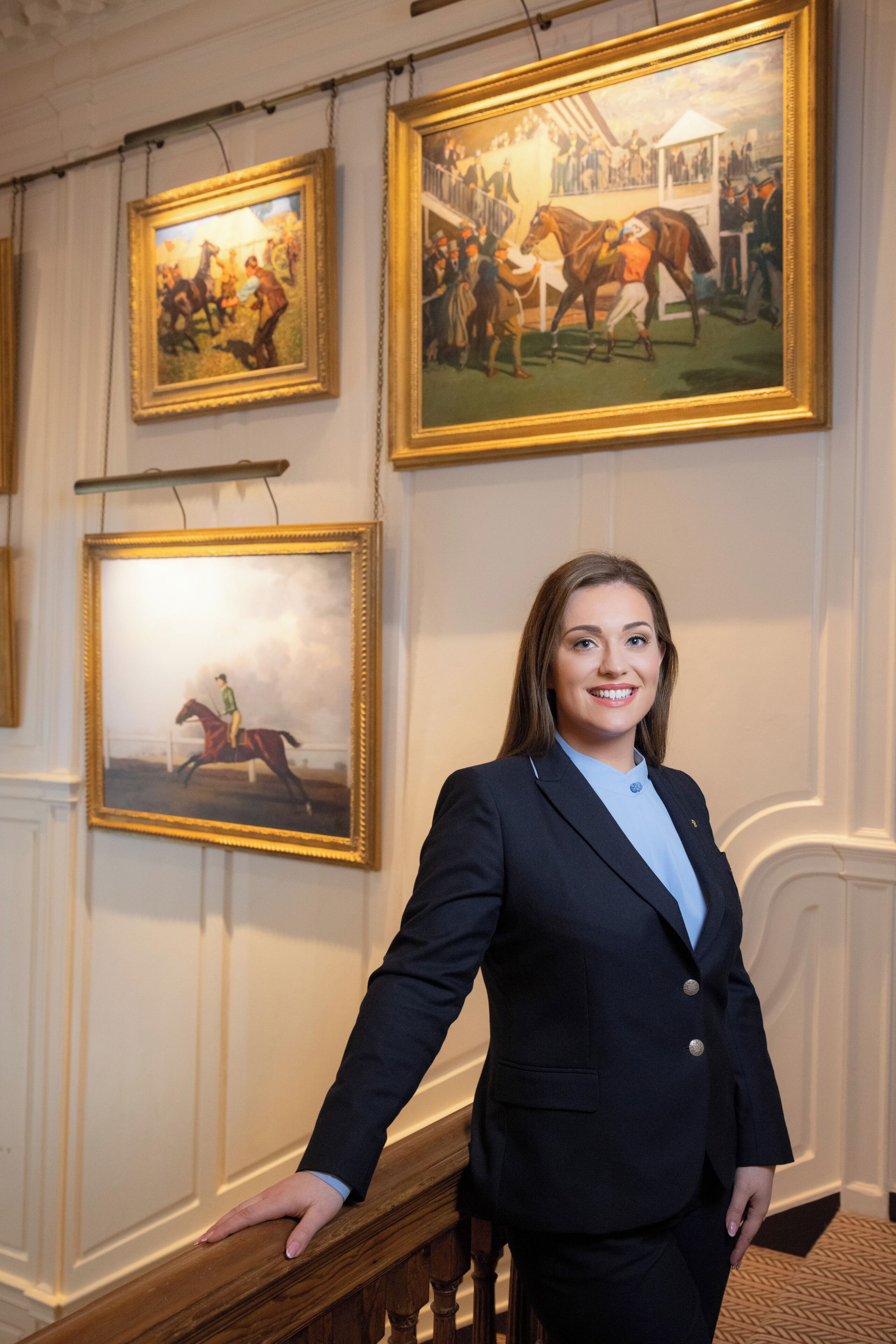 A person standing in a hallway with framed historical paintings on the walls.