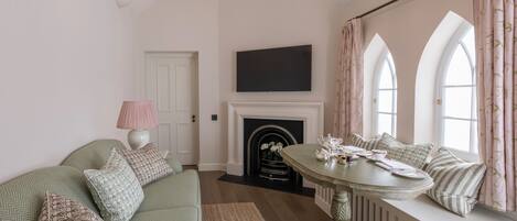 A living room with a green sofa, a fireplace, a television, and a window with curtains.
