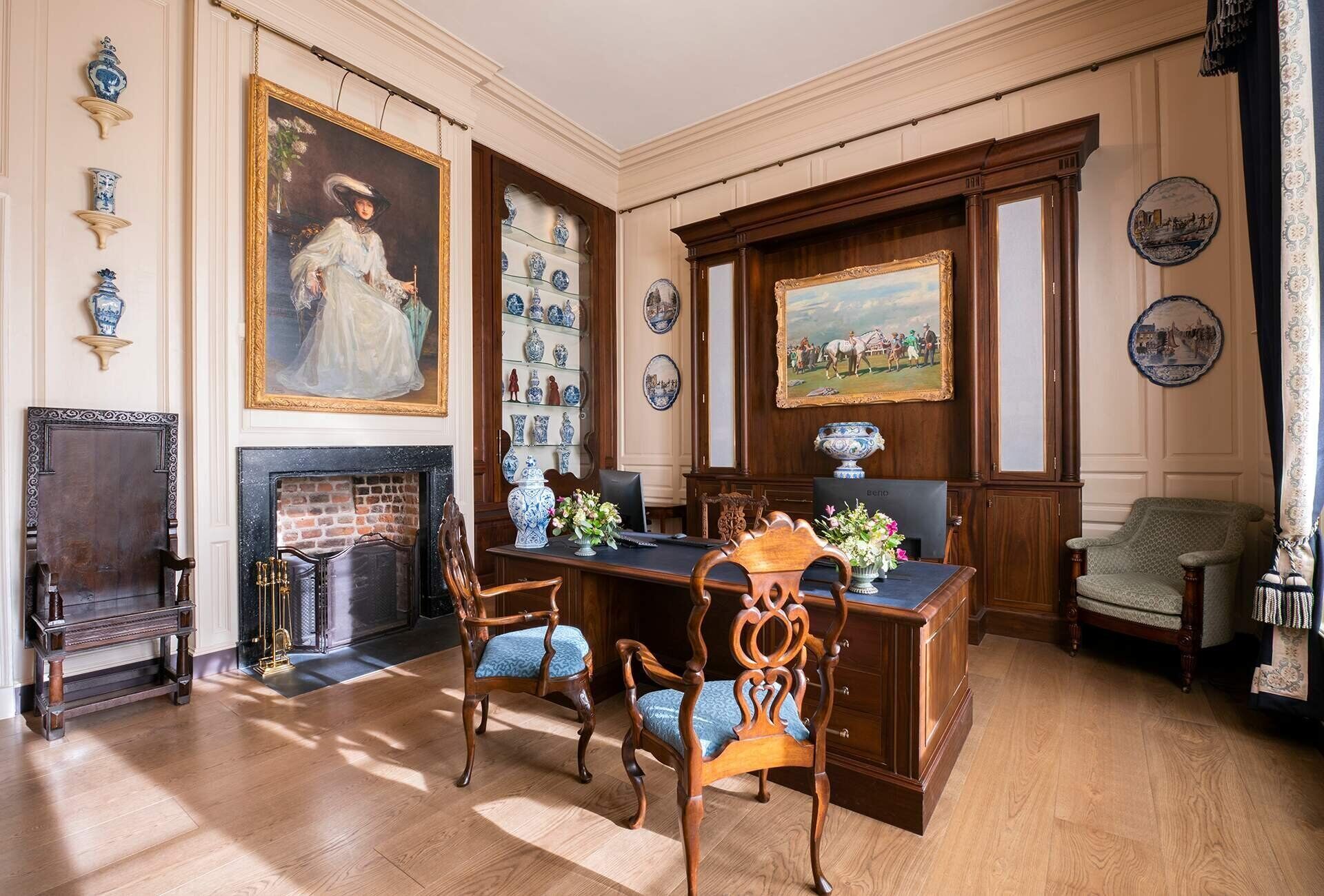 Um salão formal com lareira, mobiliário de madeira e objetos decorativos.