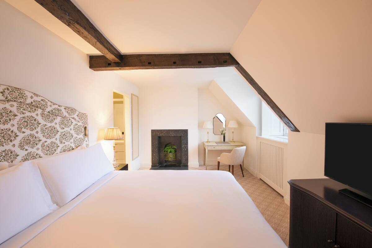 Een slaapkamer met een groot bed, een bureau, een stoel, een open haard en een televisie.
