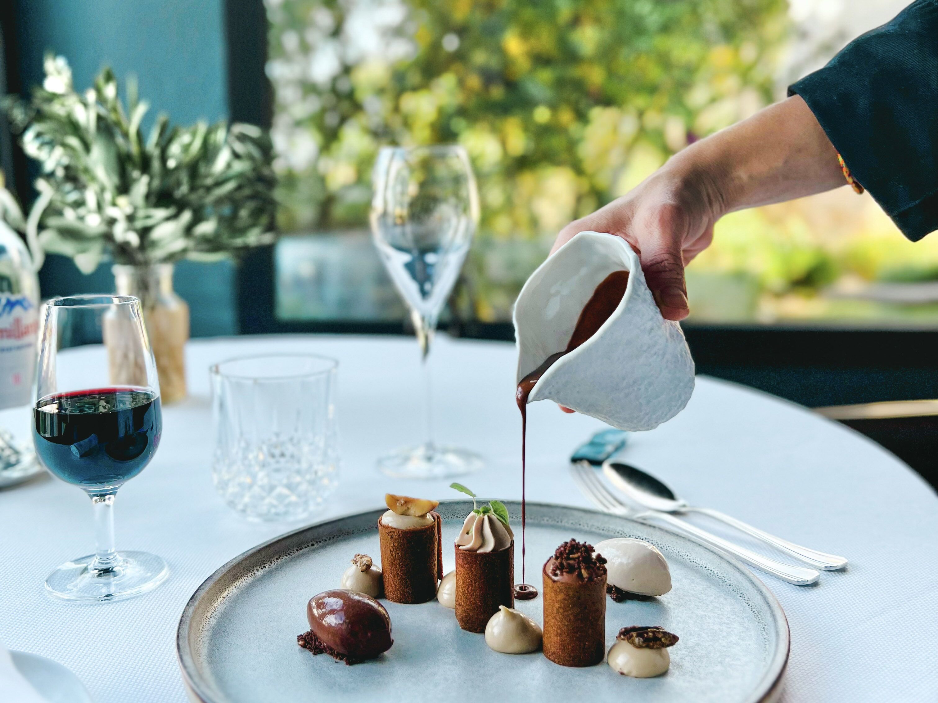 Una mesa de postres con diversos dulces y una persona sirviendo un líquido sobre un postre.