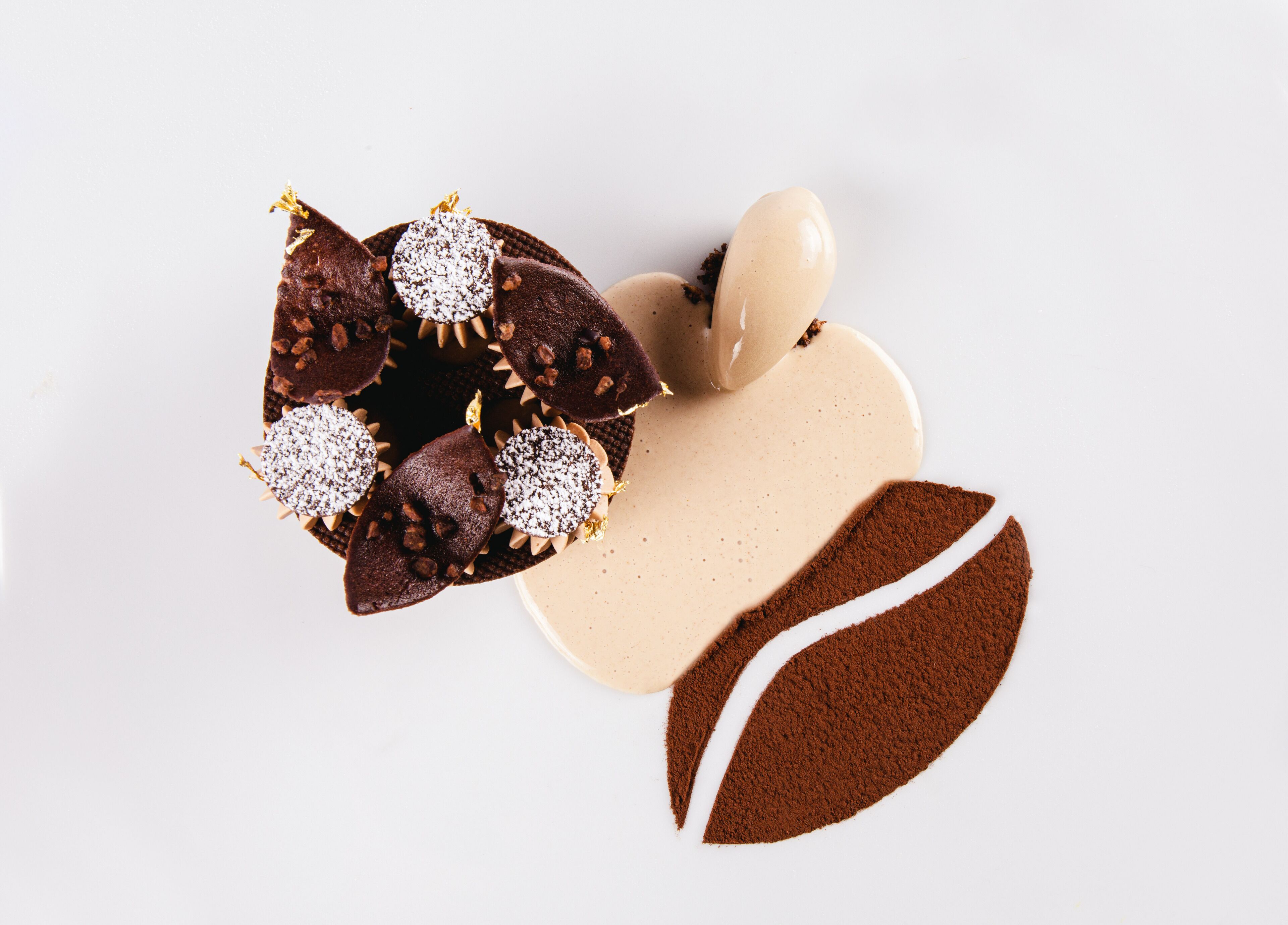 A chocolate dessert with powdered sugar and nuts, a chocolate-covered item, and a chocolate powder.