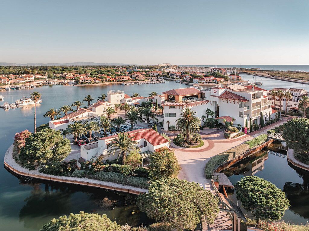 Een kustresort met een jachthaven, palmbomen en een mix van gebouwen in mediterrane stijl.