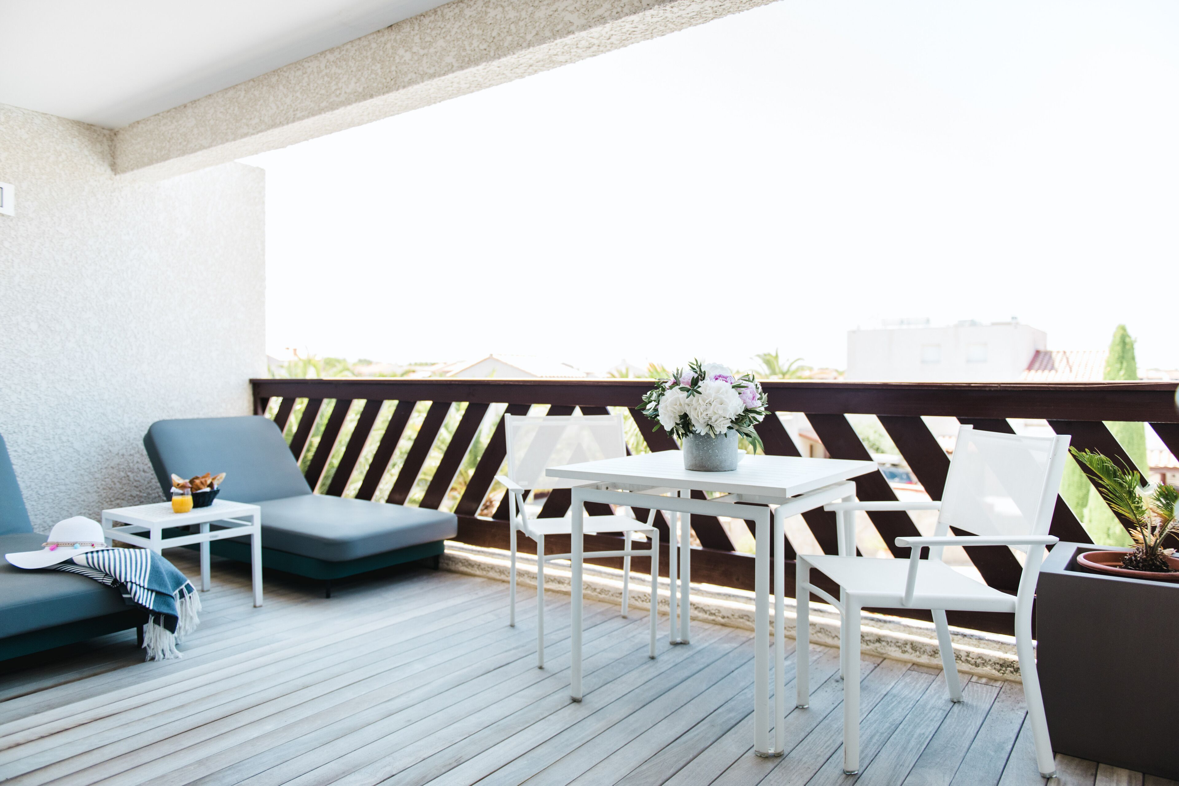 A wooden deck with a white table and chairs, a blue sofa, and a potted plant.