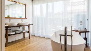 Une salle de bain moderne avec un meuble-lavabo en marbre, une baignoire sur pieds et une grande fenêtre agrémentée de rideaux légers.