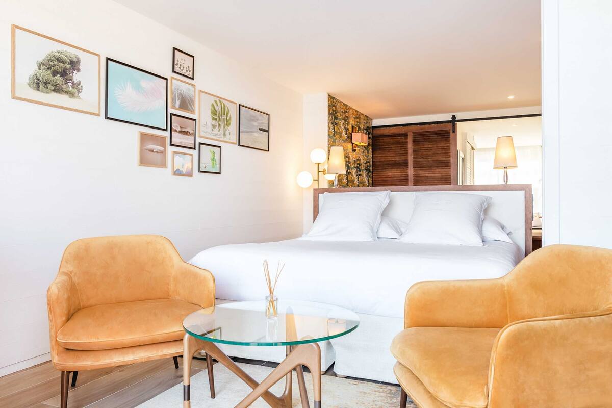 Ein modernes Hotelzimmer mit einem Bett, zwei Sesseln, einem kleinen Tisch und Wandbildern.