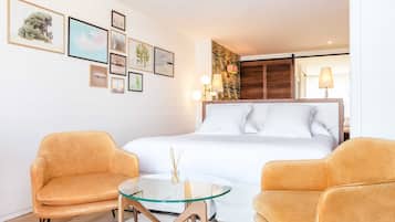 A modern hotel room with a bed, two chairs, a small table, and wall art.