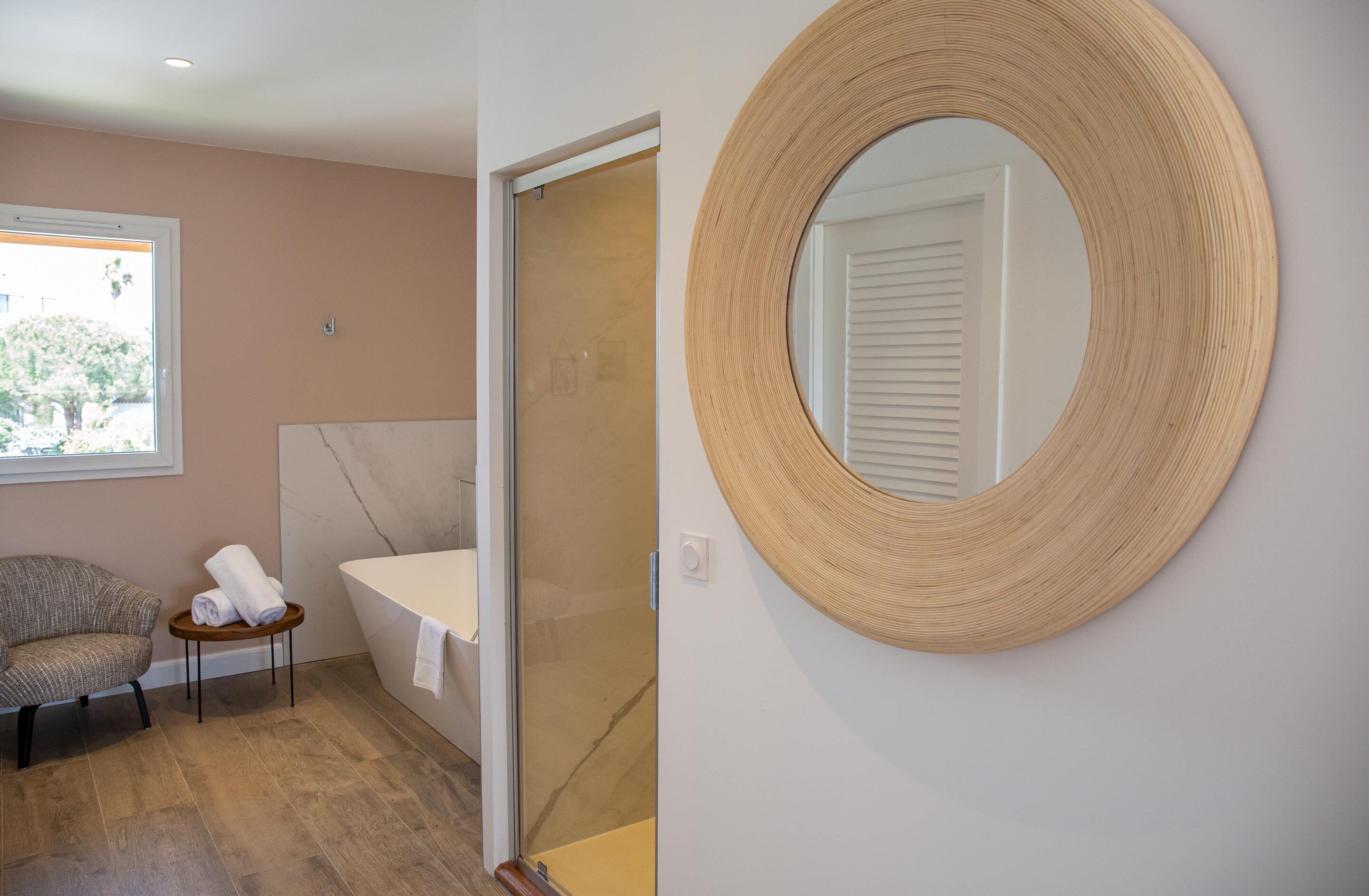 Een badkamer met een bad, een ronde spiegel, een stoel en een klein tafeltje met handdoeken.