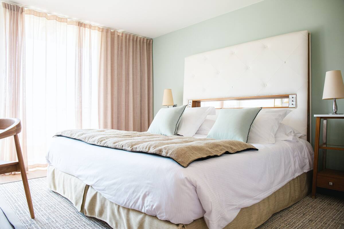 Ein Hotelzimmer mit einem großen Bett, zwei Nachttischlampen, einem Holznachttisch und einem Sessel.