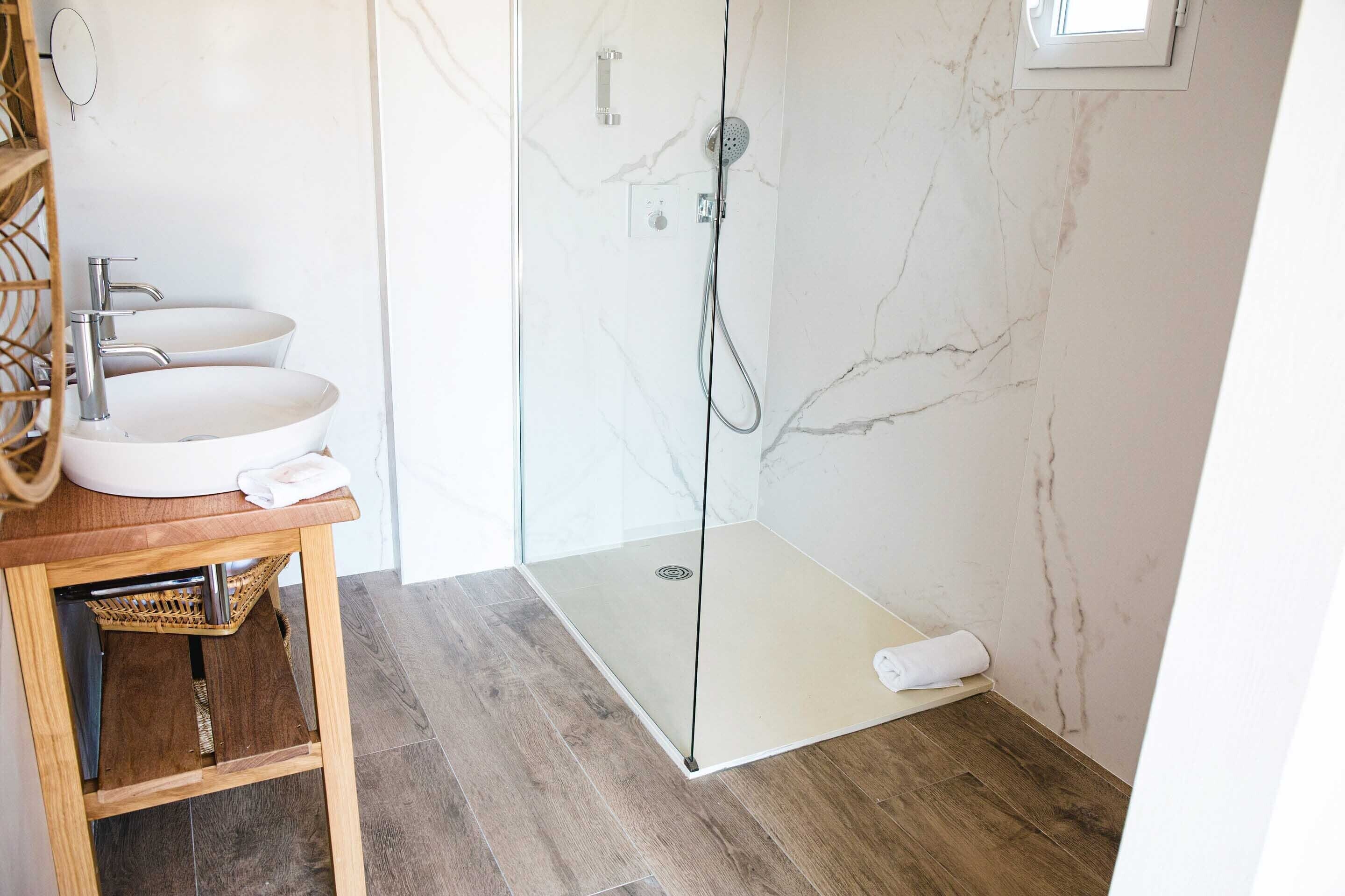 Un baño con ducha envuelta en vidrio, dos lavamanos y un mueble de tocador de madera.