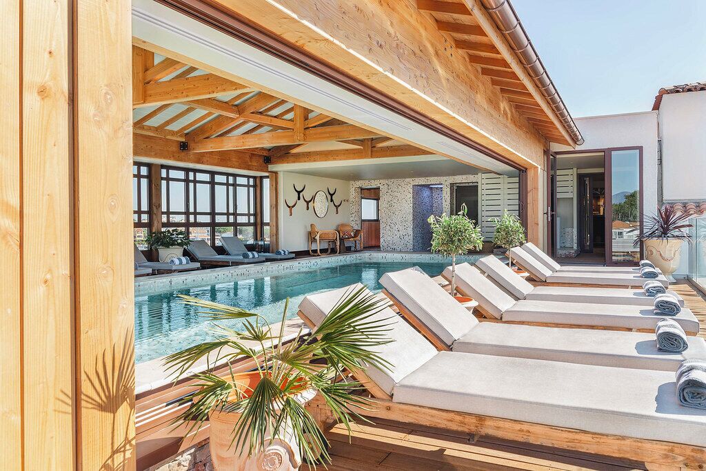 A poolside area with lounge chairs, a pool, and a wooden ceiling structure.