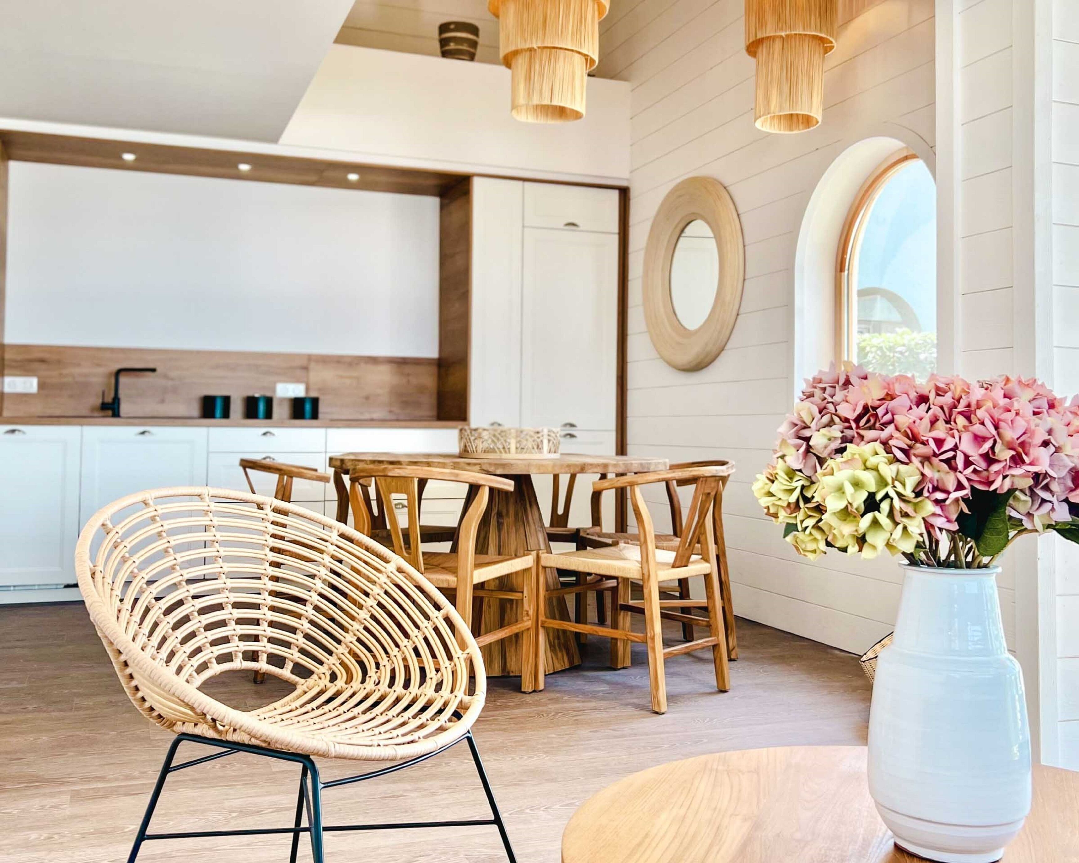 A modern kitchen with white cabinets, a wooden dining table, and a wicker chair.
