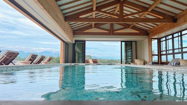 A pool area with wooden beams, lounge chairs, and a view of mountains. - Relais et Châteaux Thalasso & Spa Ile de la Lagune (Saint-Cyprien)