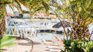 A marina with boats docked, a wooden dock, and lounge chairs. - Relais et Châteaux Thalasso & Spa Ile de la Lagune (Saint-Cyprien)