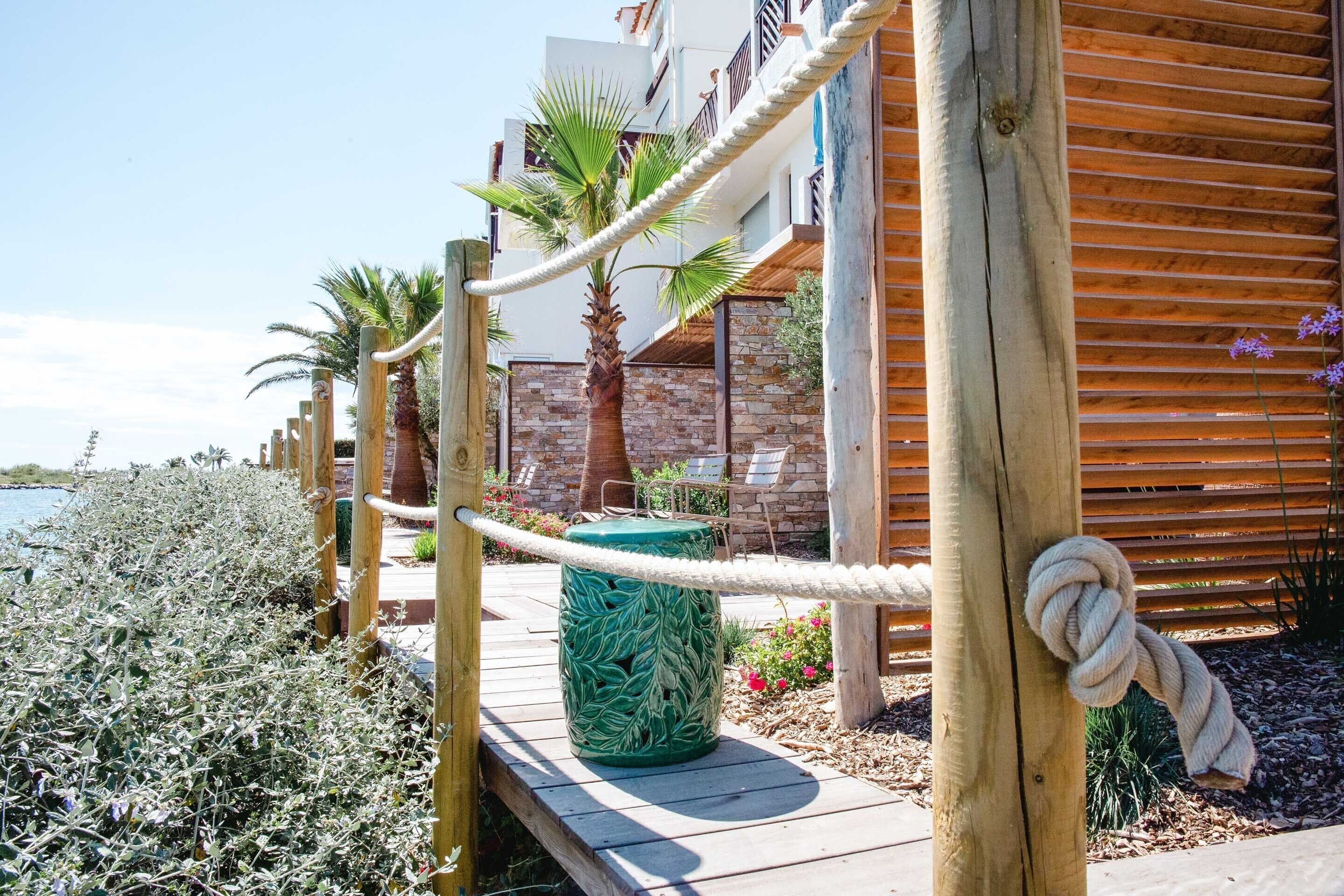 A wooden deck with a rope barrier, palm trees, and a building with a brick facade.