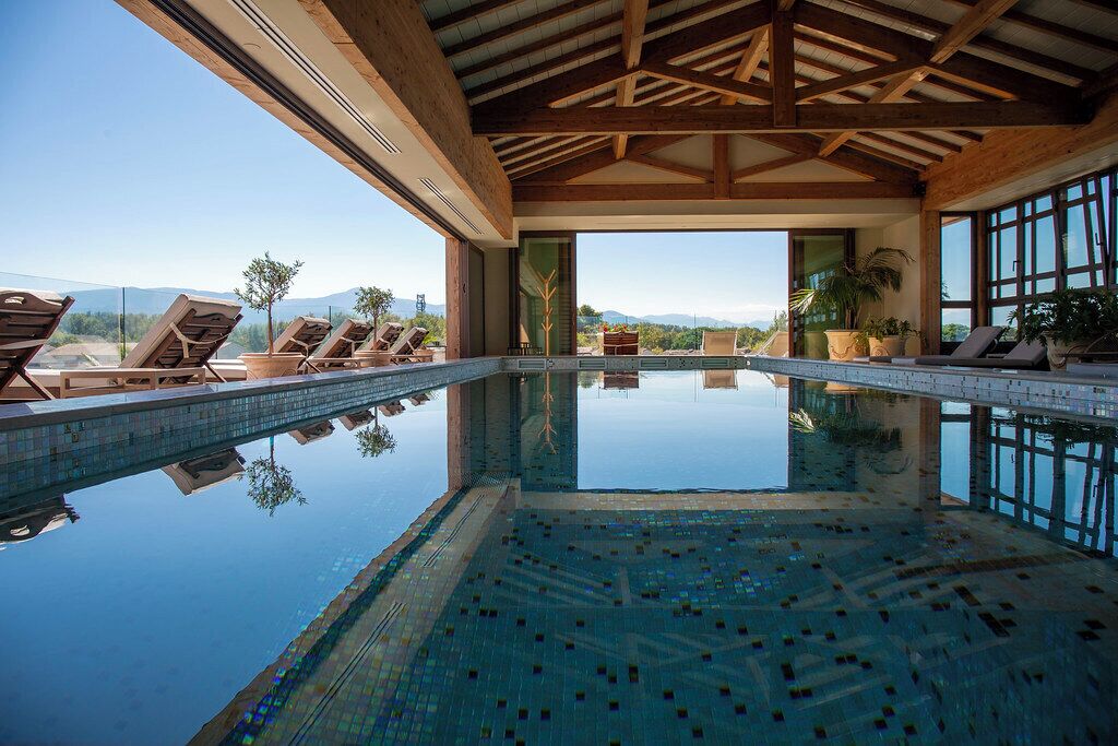 Un espace piscine doté de chaises longues, offrant une vue dégagée sur les montagnes et agrémenté d’une structure de plafond en bois.