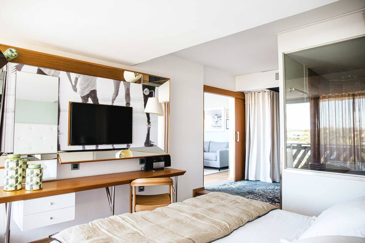 Ein Hotelzimmer mit einem Bett, einem Schreibtisch mit Computer, einem Fernseher und einem großen Spiegel.