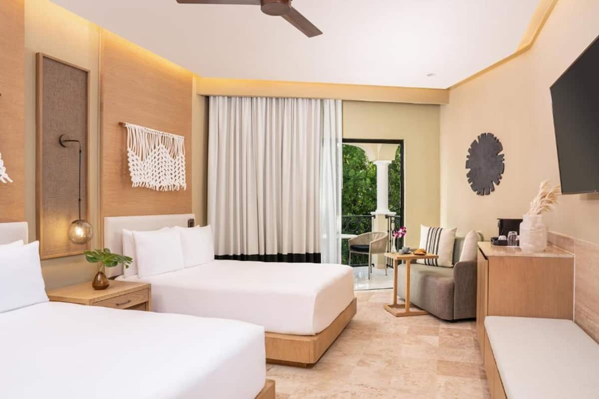 Habitación de hotel con dos camas, un balcón, un sofá y un televisor.