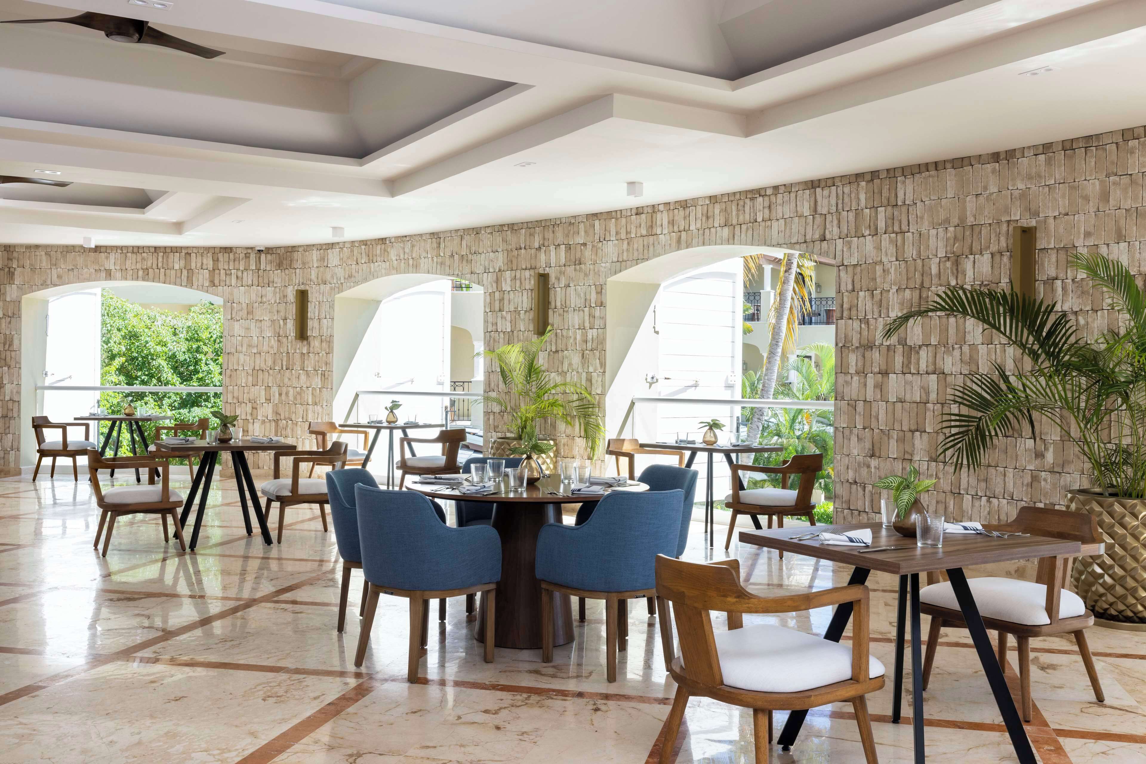 A spacious dining area with high ceilings, stone walls, and large windows offering views of greenery.