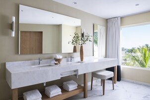 A modern bathroom with a large vanity, two sinks, a mirror, and a view of palm trees through the window.
