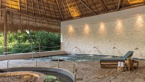 Un espace spa comprenant un bain à remous, des chaises longues et un mur de pierre agrémenté d’éléments d’eau.