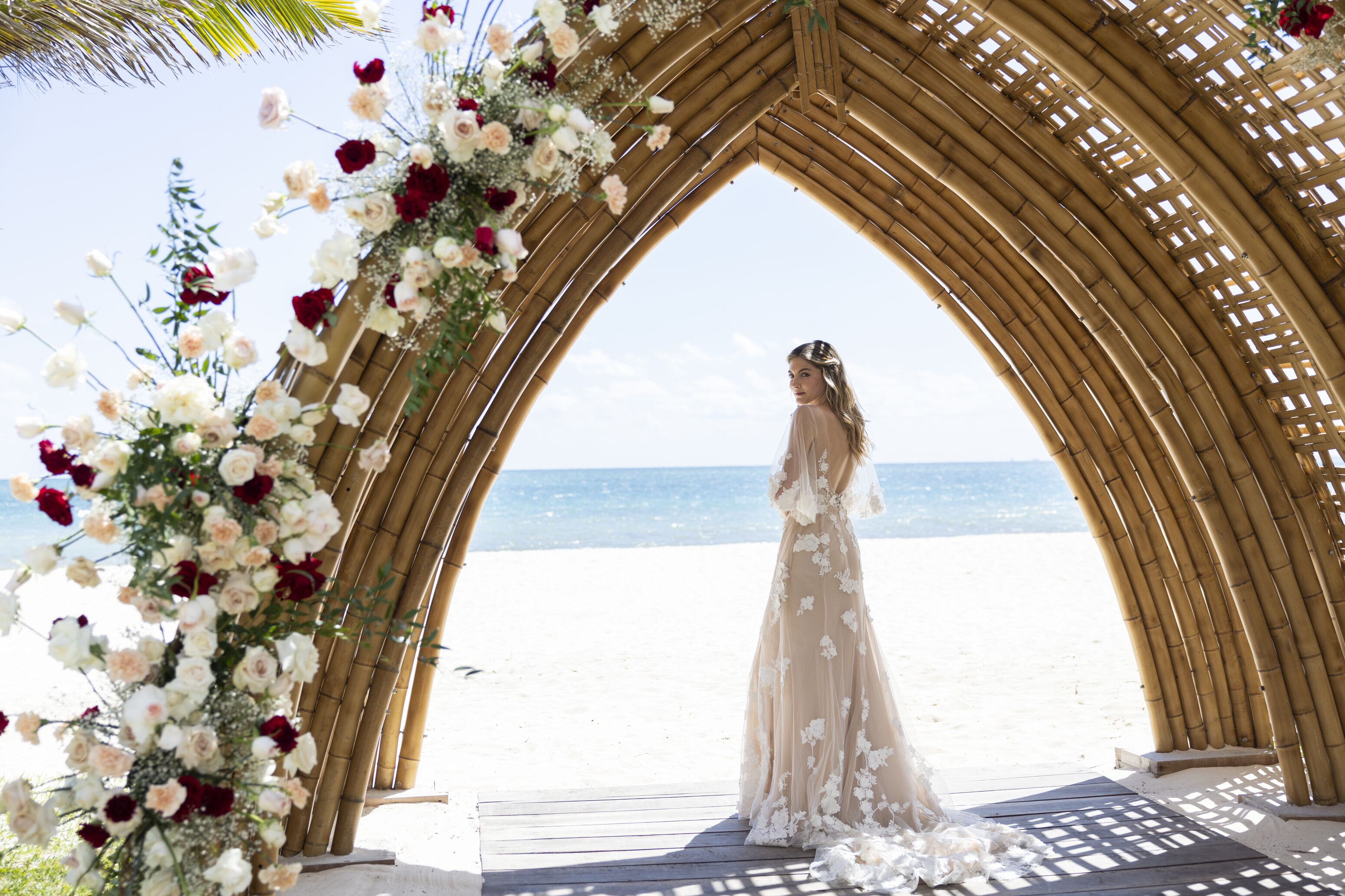 Une arche décorée de fleurs pour un mariage sur la plage, avec une mariée portant une robe de mariée.