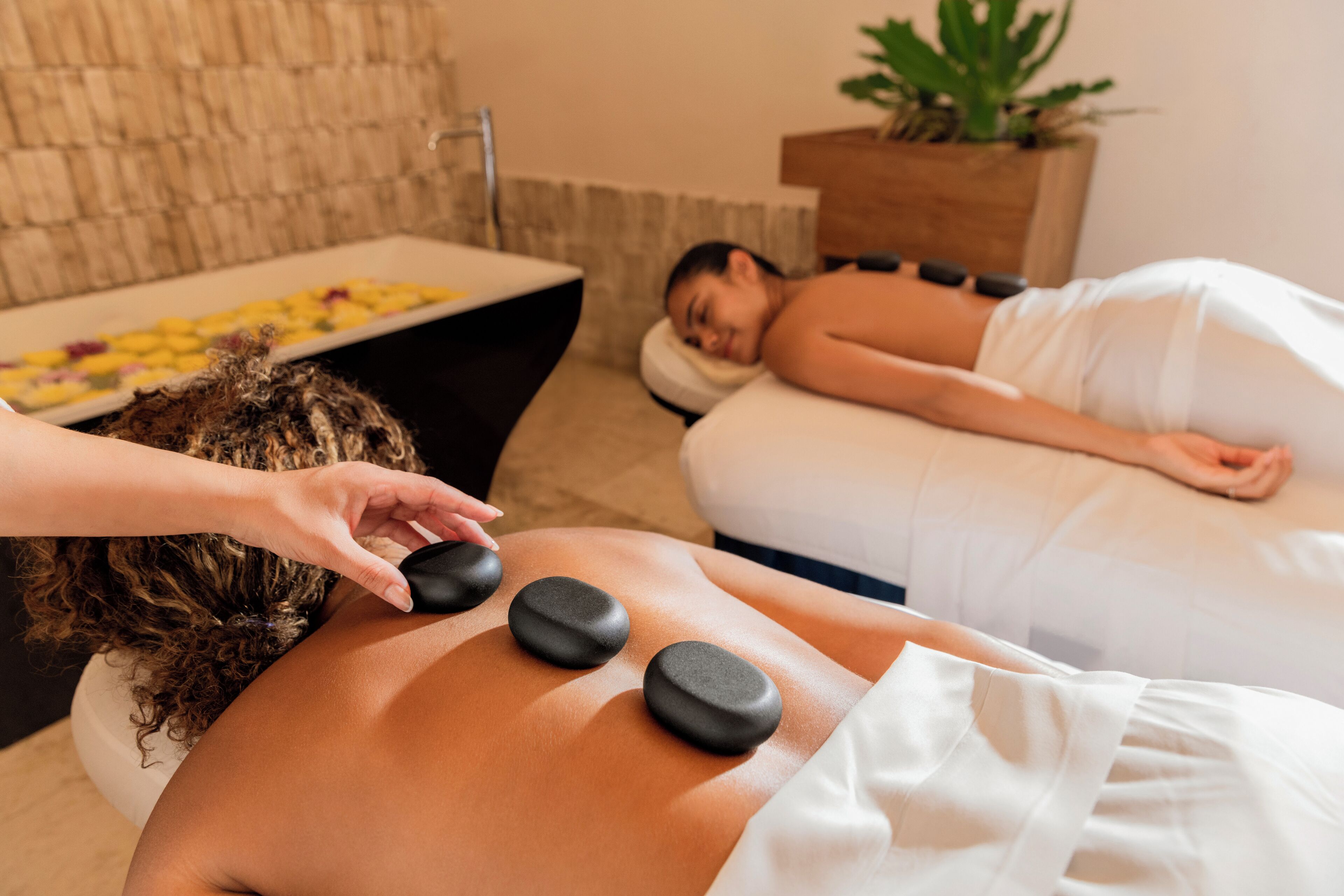 Seduta di massoterapia in una spa, con lettino da massaggio, una persona che riceve un massaggio alla schiena e un vassoio con pietre di massaggio.