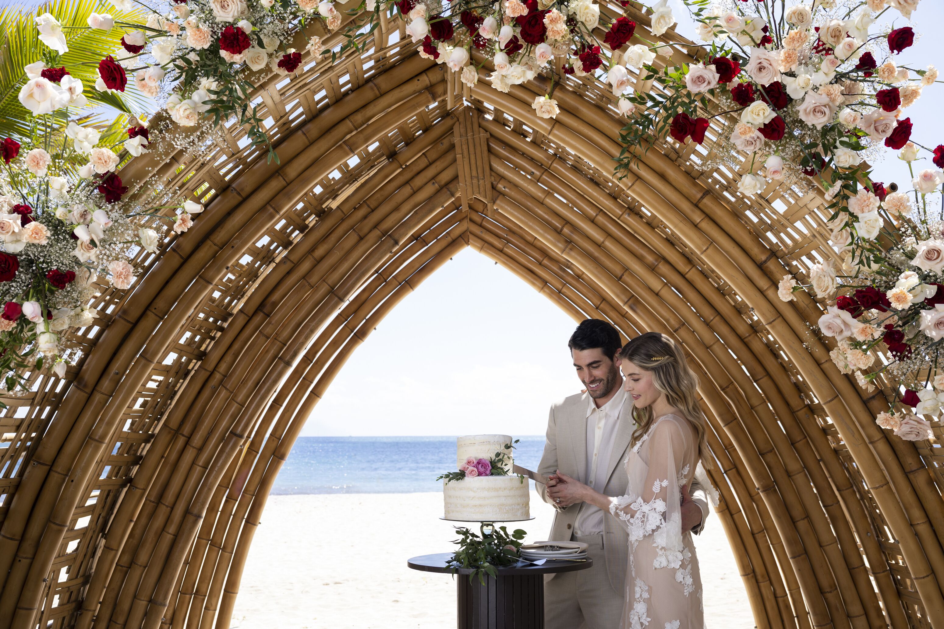 Eine Hochzeitszeremonie an einem Strand, mit einem Blumengesteckten Bogen aus Bambus.
