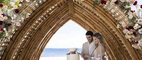 Una ceremonia de boda en un espacio frente al mar, con un arco de bambú decorado con flores.