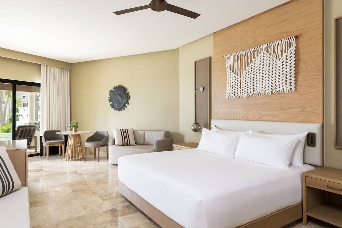 Habitación de hotel con una cama grande, un ventilador de techo, una mesa redonda con sillas y vistas al exterior.
