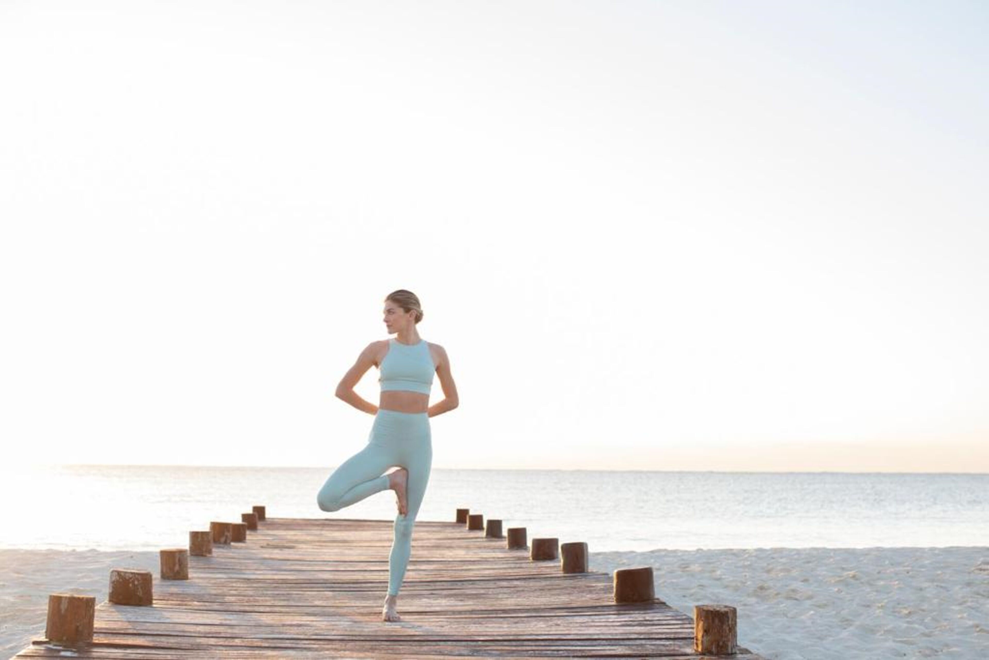 A person performing a yoga pose on a wooden pier extending into a beach.