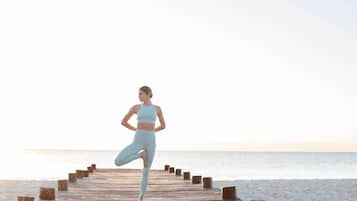 A person performing a yoga pose on a wooden pier extending into a beach.