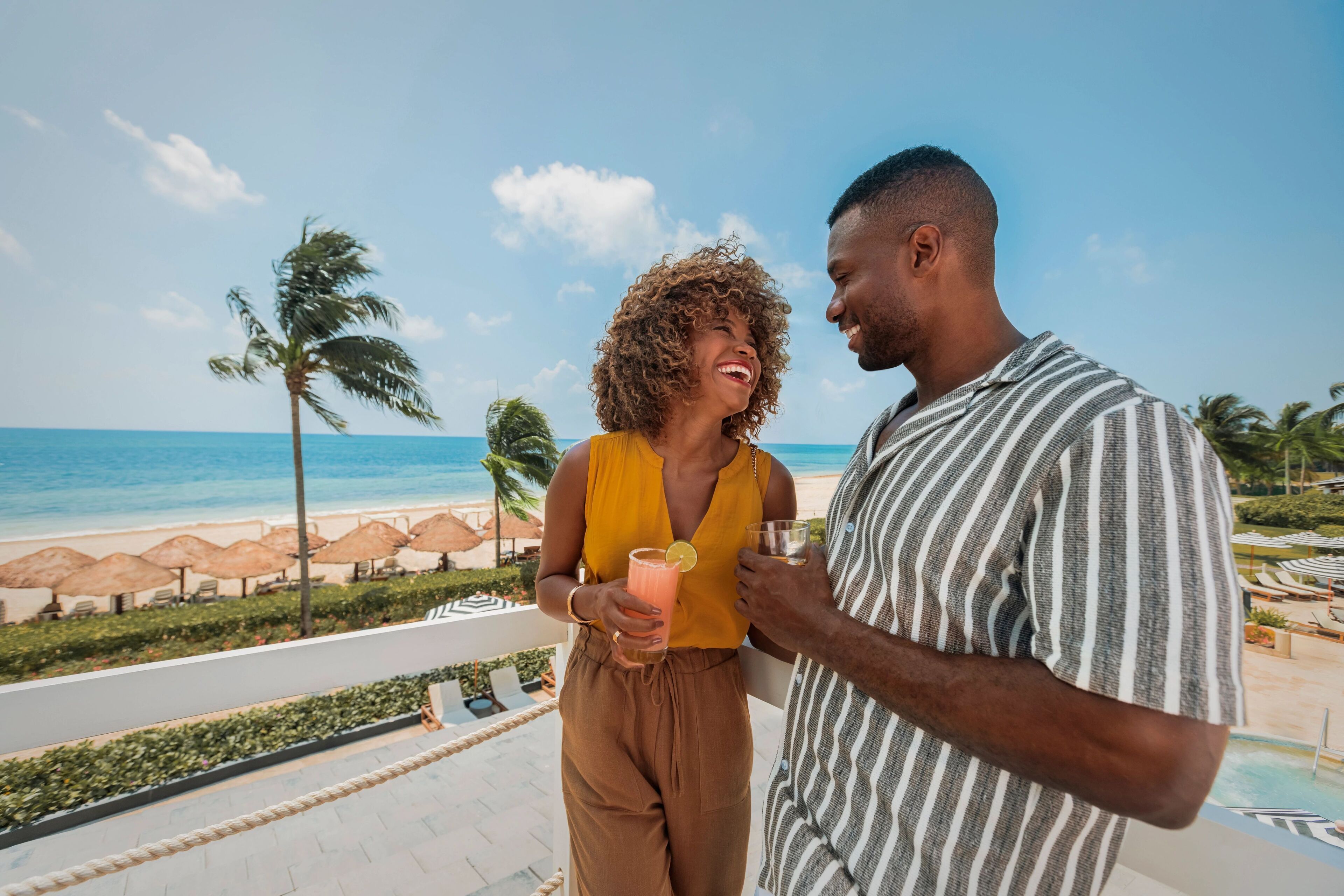 Un couple sur un balcon donnant sur la plage, avec vue sur l’océan et les palmiers.