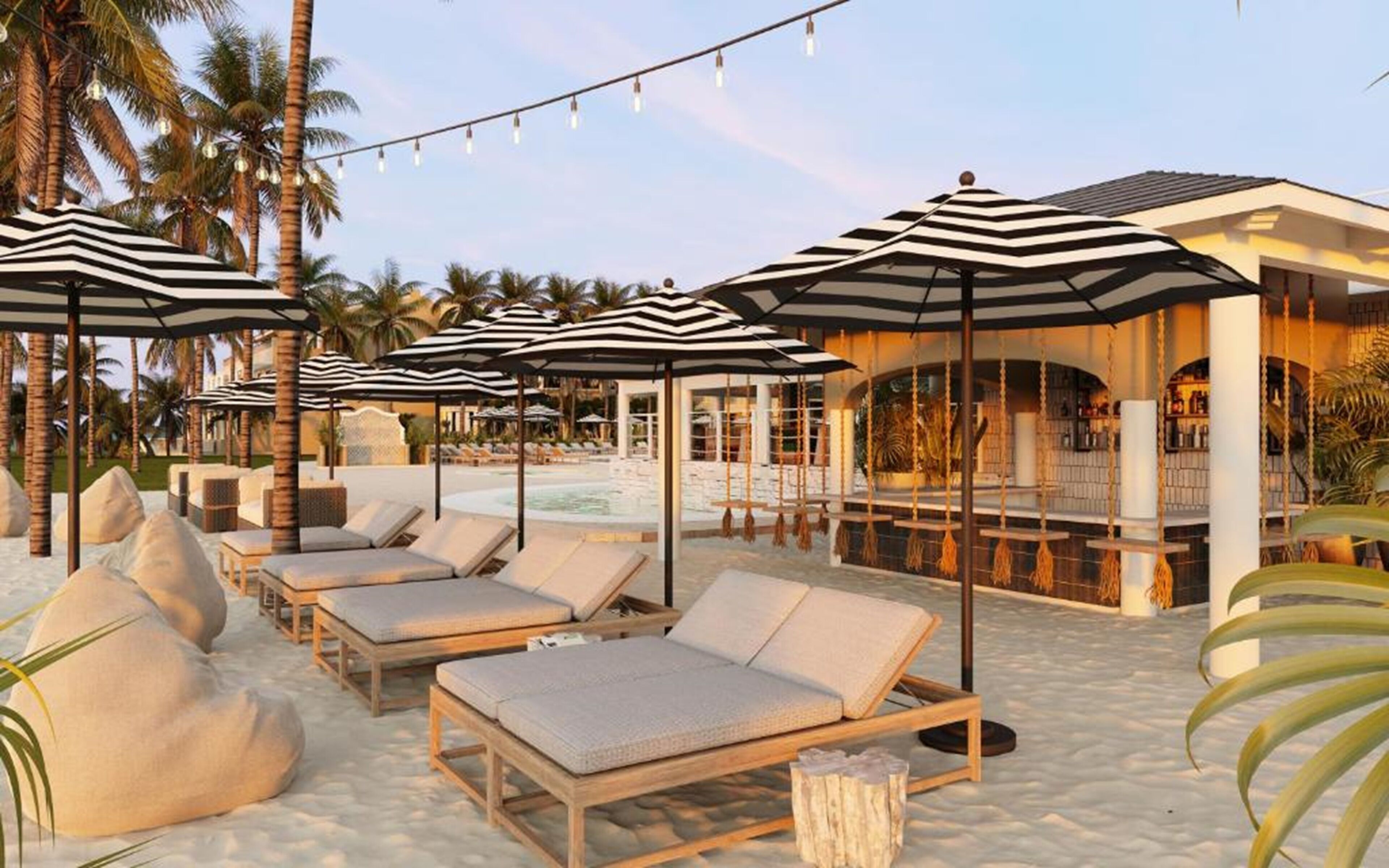 Un complexe hôtelier doté de chaises longues et de parasols à rayures sur une plage de sable, d’une piscine et d’un espace bar à l’ambiance tropicale.