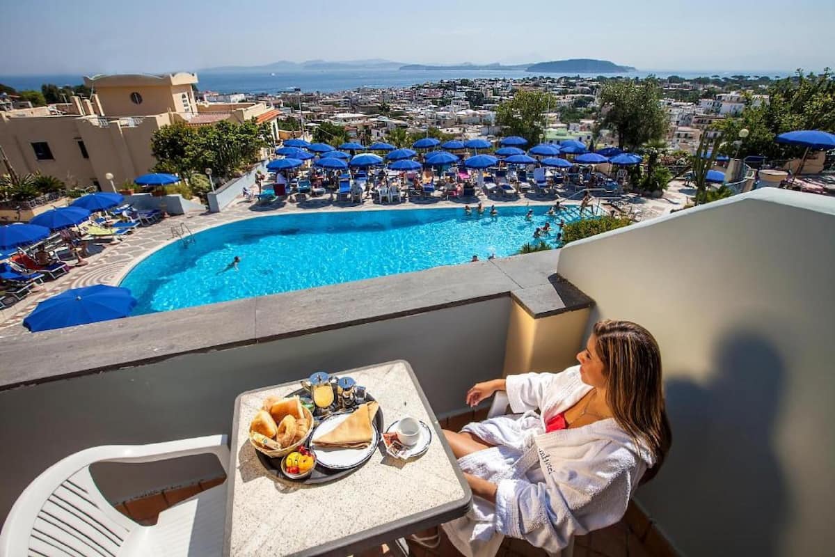 A poolside view with a table set for breakfast, a pool, and a cityscape in the background.