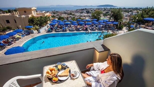 A poolside view with a table set for breakfast, a pool, and a cityscape in the background. - Hotel Terme President (Ischia)