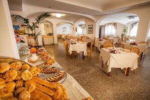 Un espace repas comprenant plusieurs tables, des chaises et un buffet où sont disposés du pain et des viennoiseries.