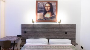 A hotel room with a wooden headboard, a bed with white linens, a desk with a telephone, and a framed artwork above the bed. - Hôtel Léonard de Vinci (Paris)