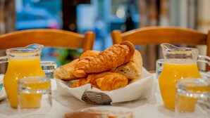 A breakfast setting with croissants, orange juice, and a basket on a table. - Hôtel Léonard de Vinci (Paris)