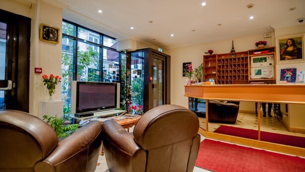 A modern hotel lobby with leather seating, a TV, a bookshelf, and a large window offering a view of the city. - Hôtel Léonard de Vinci (Paris)