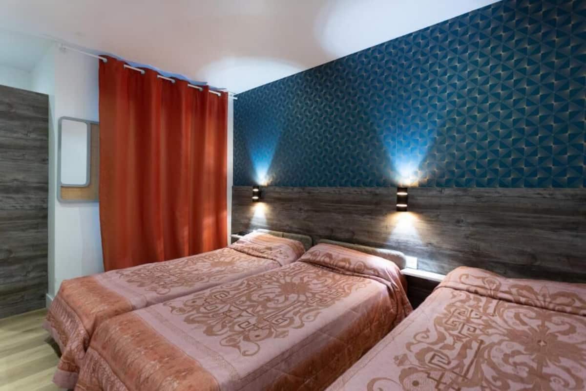 A room with two beds, a wooden headboard, a red curtain, and a blue patterned wall.