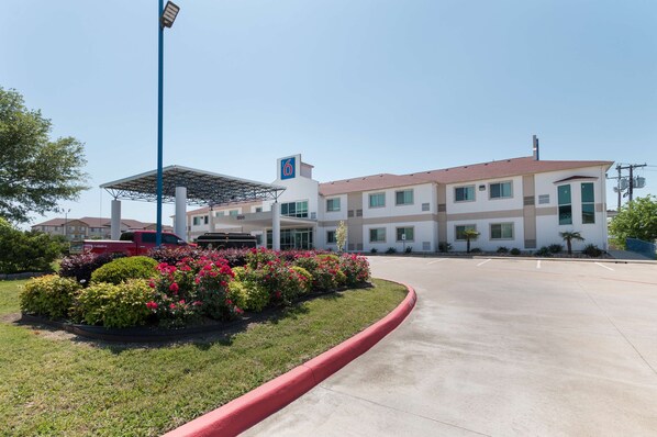A modern hotel with a parking lot, a covered parking area, and a landscaped garden with colorful flowers.
