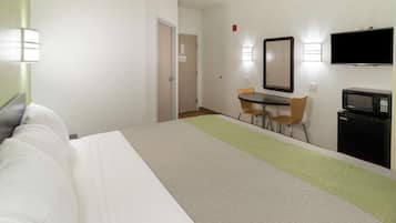 Quarto de hotel com uma cama, uma escrivaninha com cadeira, televisão e micro-ondas.