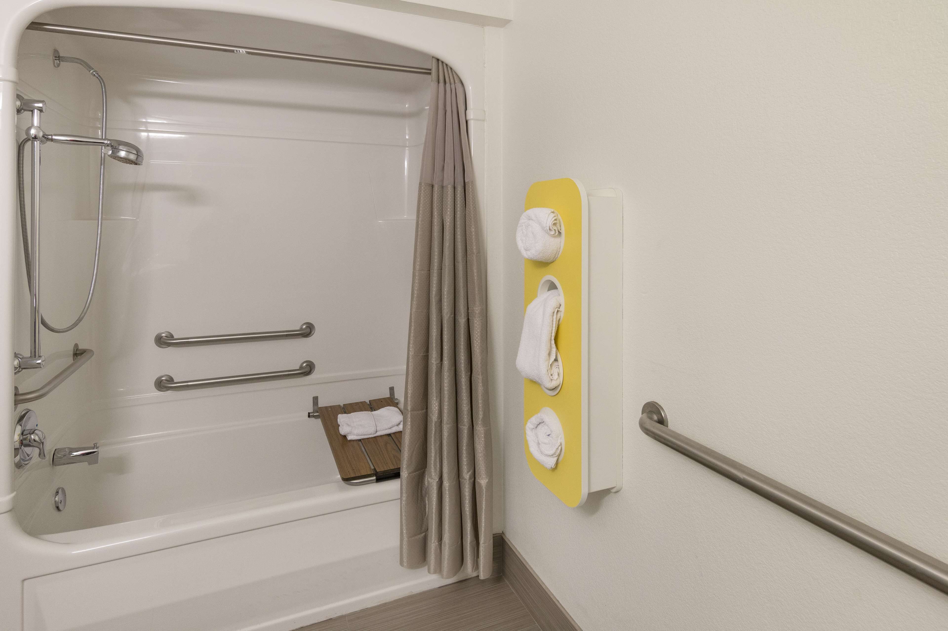 A modern bathroom with a bathtub, grab bars, and a towel rack.